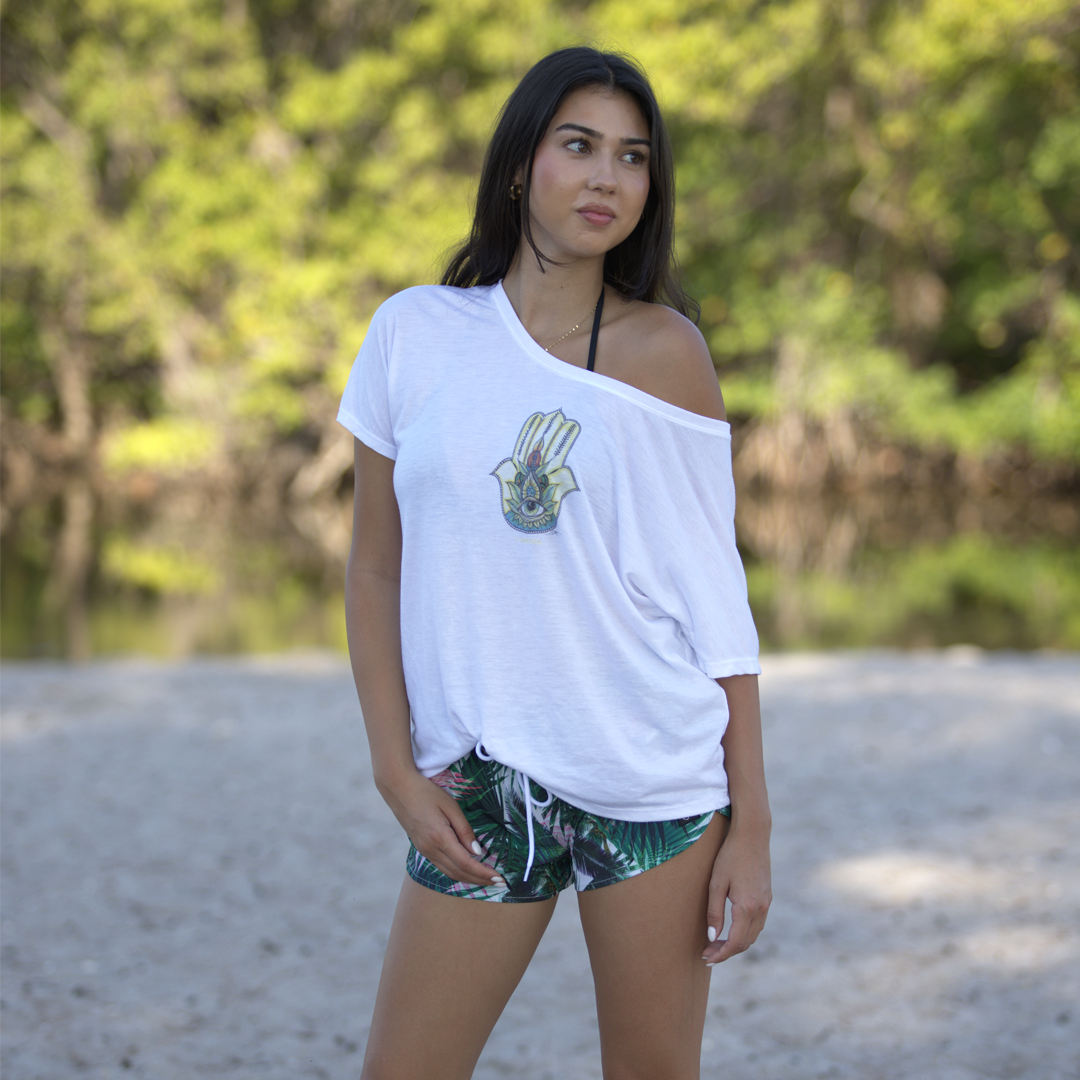 Person wearing a white scoop neck t-shirt with a colorful Hamsa hand design outdoors.