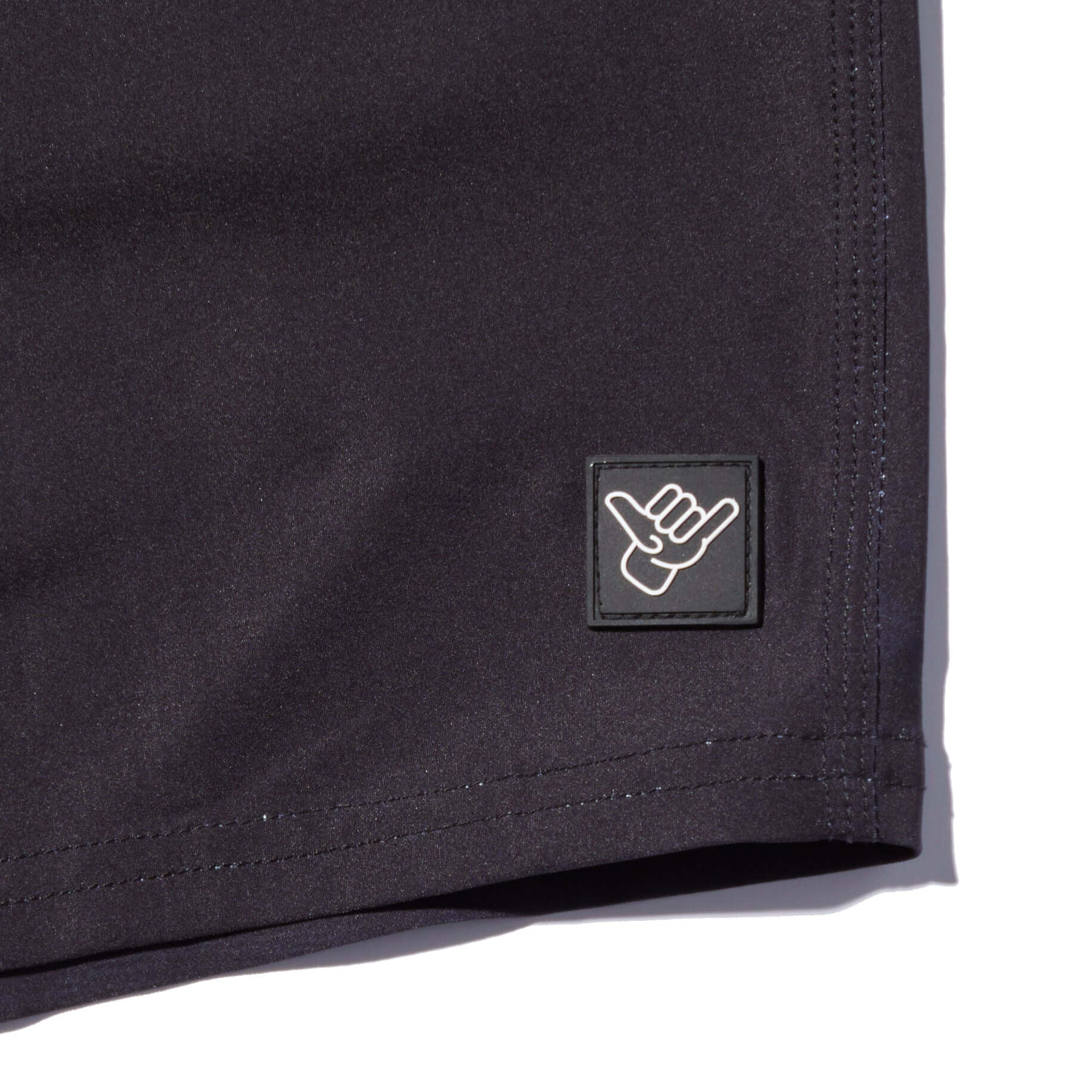 Close-up of the DaveL Manu Volley Short featuring a black fabric and signature logo patch.