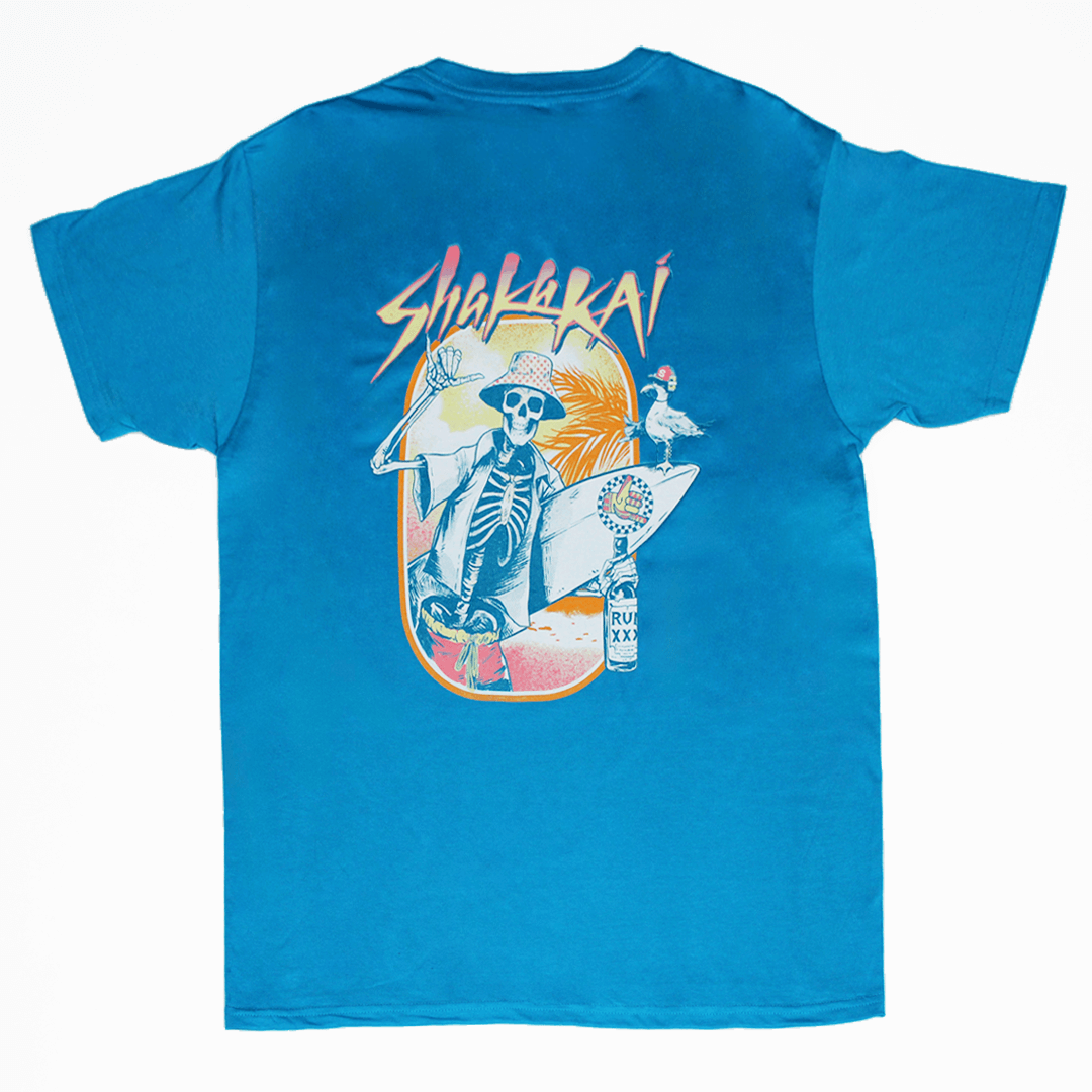 Blue t-shirt with a skeleton holding a surfboard and 'Shaka Kai' branding on a white background