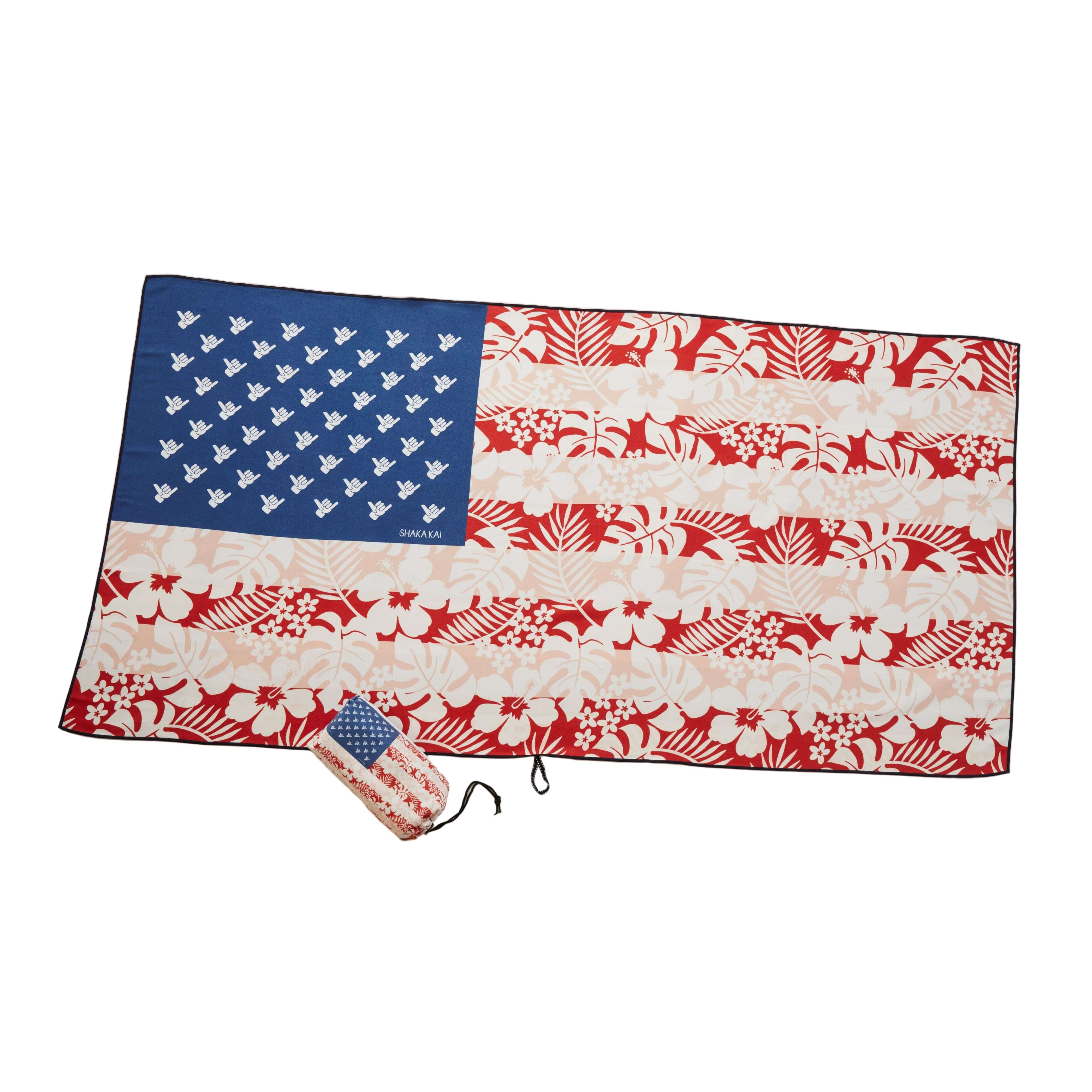 An oversized beach towel with a geometric pattern featuring red, white, and blue colors, laid out flat with a matching small bag.