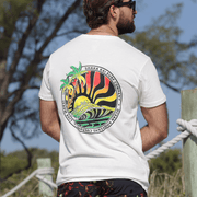 Man wearing a Rasta Wave T-Shirt featuring vibrant wave graphic and palm trees against a sunny backdrop.