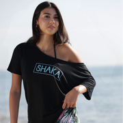 Woman wearing a black scoop neck t-shirt with 'SHAKA' text at the beach